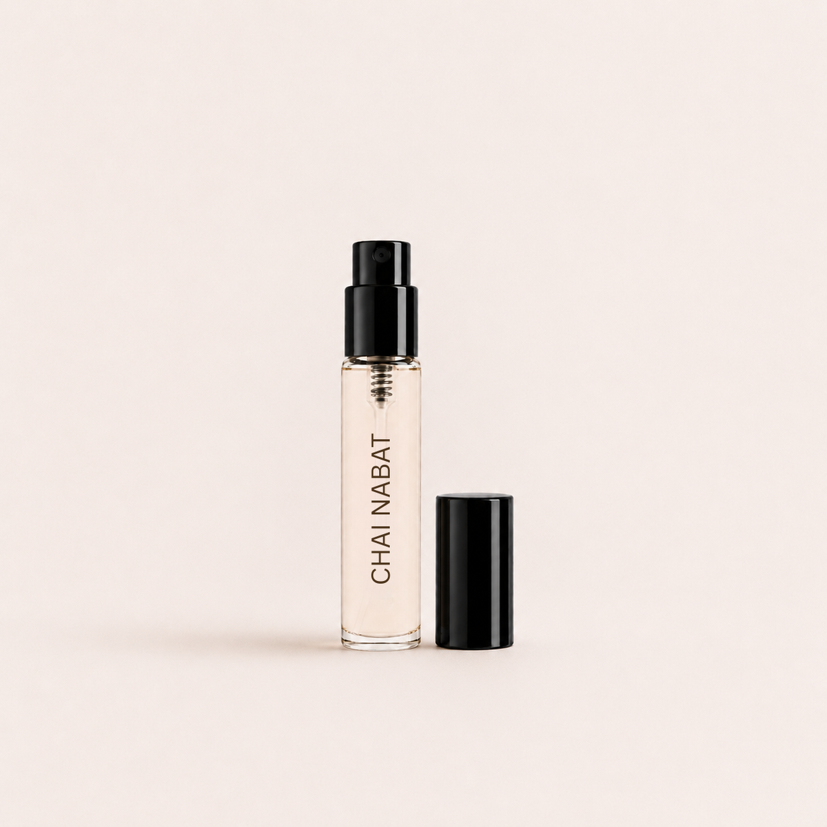 A clear glass perfume or fragrance atomizer bottle labeled 'CHAI NABAT' in black text, with a black spray top and matching black cap, shown on a warm off-white background.