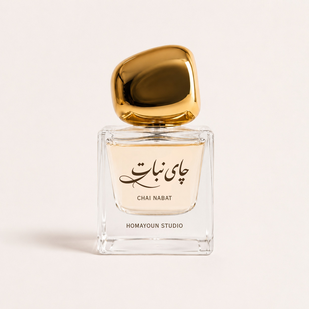 A square clear glass perfume bottle with pale warm liquid, a glossy metallic gold cap, and black Arabic script with the text 'CHAI NABAT' and 'HOMAYOUN STUDIO' on the front, centered on a light warm beige background.